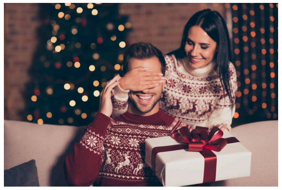 Una mujer cubre los ojos de un hombre mientras sostiene un regalo de navidad